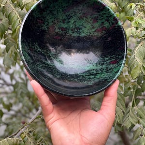 May include: A green and black bowl made of polished stone. The bowl has a swirling pattern of green and black with hints of pink.