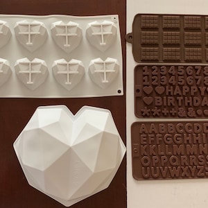 May include: A collection of silicone molds for crafting. Includes a white geometric heart mold, a white tray with heart-shaped molds, and brown molds for chocolate bars, numbers, letters, and symbols. Ideal for DIY projects.