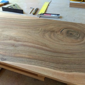 Puede incluir: Primer plano de una mesa de madera de color marr&oacute;n claro con un nudo grande en el centro. La veta de la madera es visible y tiene un aspecto natural y r&uacute;stico.