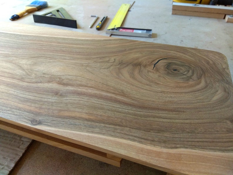 Puede incluir: Primer plano de una mesa de madera de color marr&oacute;n claro con un nudo grande en el centro. La veta de la madera es visible y tiene un aspecto natural y r&uacute;stico.