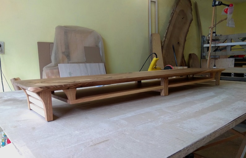 Puede incluir: Una estanter&iacute;a larga de madera con dos niveles. La estanter&iacute;a est&aacute; hecha de madera natural con un acabado r&uacute;stico. La estanter&iacute;a est&aacute; soportada por cuatro patas y tiene un borde ligeramente curvado.