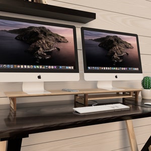 Puede incluir: Dos ordenadores iMac blancos con biseles negros est&aacute;n sobre un soporte de monitor de madera. Los ordenadores est&aacute;n sobre un escritorio marr&oacute;n oscuro con un teclado blanco y un rat&oacute;n blanco. Un peque&ntilde;o cactus en maceta est&aacute; sobre el escritorio a la derecha de los ordenadores.