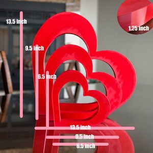 May include: Three red heart-shaped nesting boxes, the largest is 13.5 inches tall and 9.5 inches wide, the middle is 9.5 inches tall and 6.5 inches wide, and the smallest is 6.5 inches tall and 6.5 inches wide. The boxes are made of a thick, sturdy material and have a smooth, glossy finish.