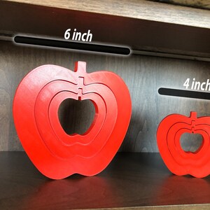 May include: Two red wooden apple shaped nesting toys. The larger apple is 15 cm wide and the smaller apple is 10 cm wide.
