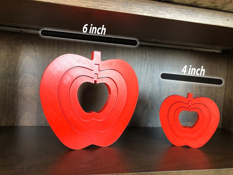 May include: Two red wooden apple shaped nesting toys. The larger apple is 15 cm wide and the smaller apple is 10 cm wide.