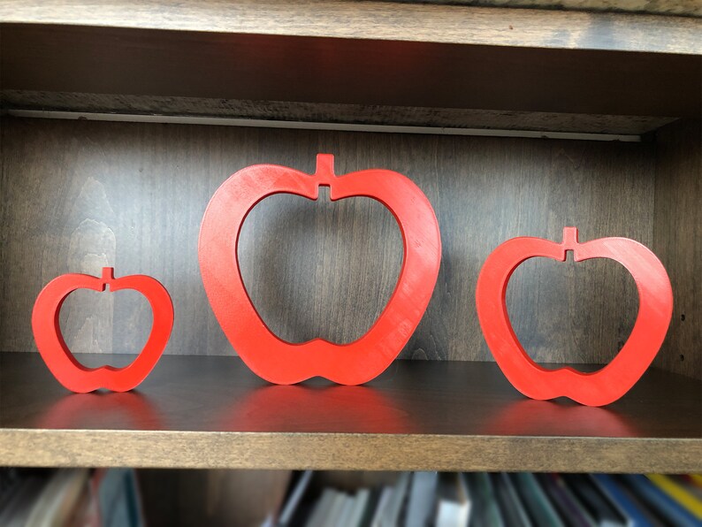 May include: Three red apple-shaped wall decorations of varying sizes on a wooden shelf.
