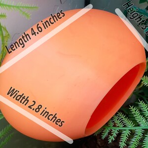 May include: A bright orange, hollow, plastic egg-shaped object with a large opening on one side. The object measures 4.6 inches in length, 2.8 inches in width, and 3 inches in height.