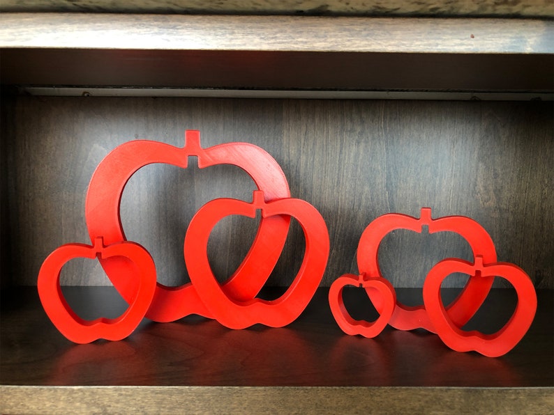 May include: A set of five red wooden apple-shaped ornaments. The ornaments are nested inside each other, with the largest at the back and the smallest at the front.