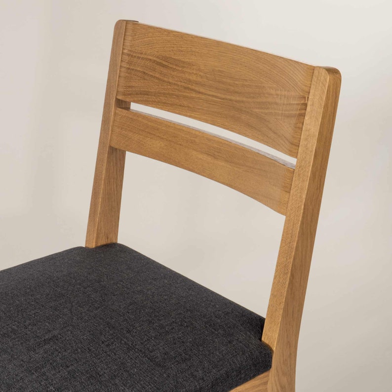 May include: A wooden chair with a dark gray fabric seat. The chair has a simple design with a curved back and a single slat across the back.
