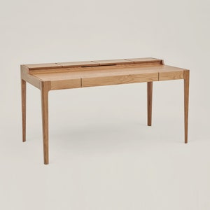 May include: A light wood desk with four drawers and a raised lip on the front edge. The desk has a simple, modern design with straight lines and a natural wood finish.