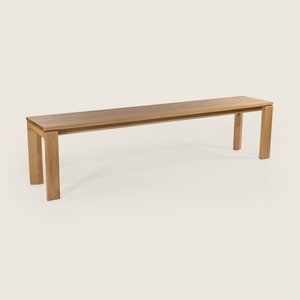 May include: A long, wooden bench with a natural finish. The bench has a simple, rectangular design with four legs.