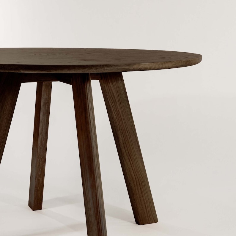 May include: A dark brown wooden table with a round top and four legs. The table is made of solid wood and has a natural finish.
