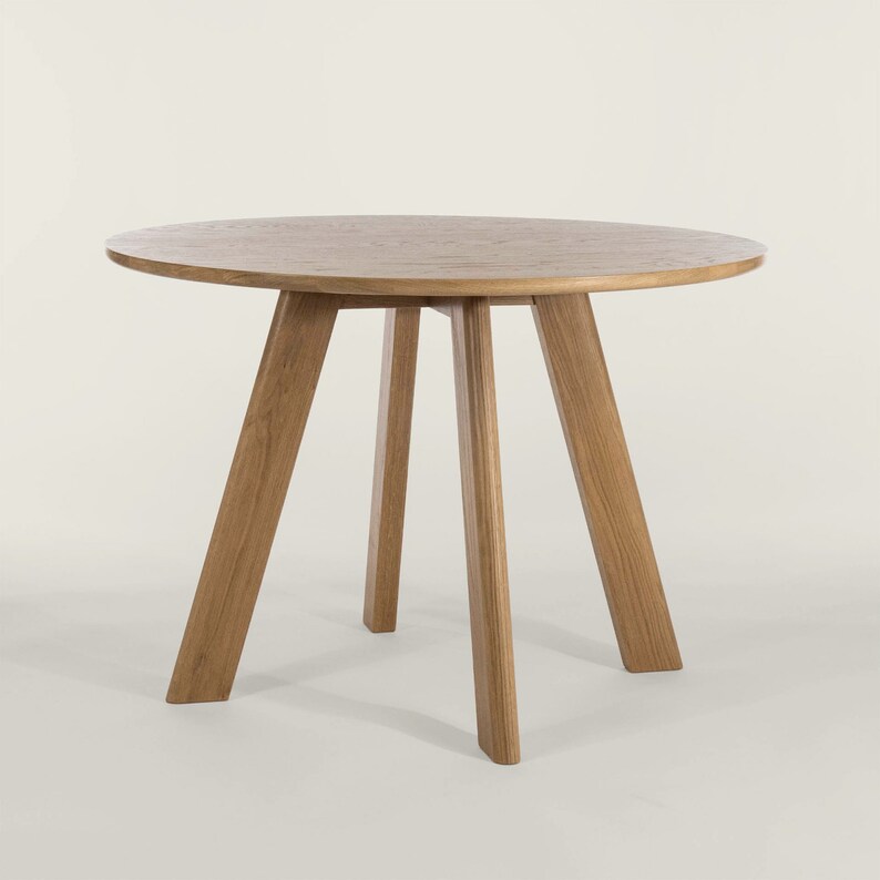 May include: A round wooden table with a light brown finish and three legs. The table is made of solid wood and has a simple, modern design.