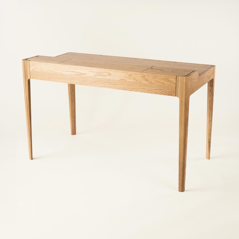 May include: A light wood desk with a simple design. The desk has a rectangular top with two small drawers on the right side. The desk has four legs that are slightly curved.
