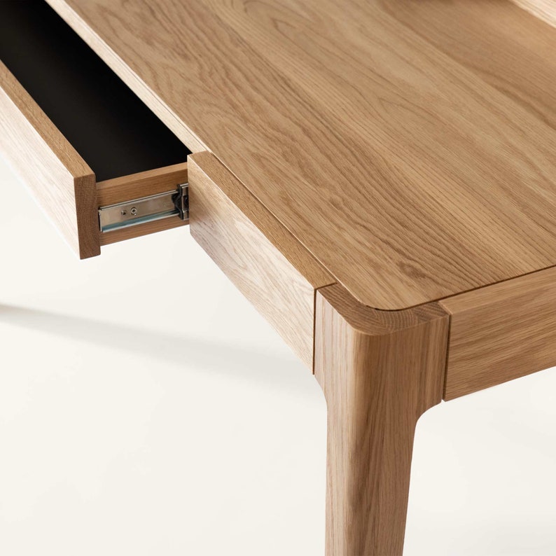 May include: A light wood desk with a drawer that is open. The desk has a simple design with clean lines and a natural wood finish.