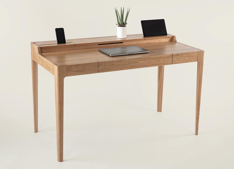 May include: A light wood desk with two drawers and a built-in shelf for a laptop or tablet. The desk has a modern design with sleek lines and a minimalist aesthetic.