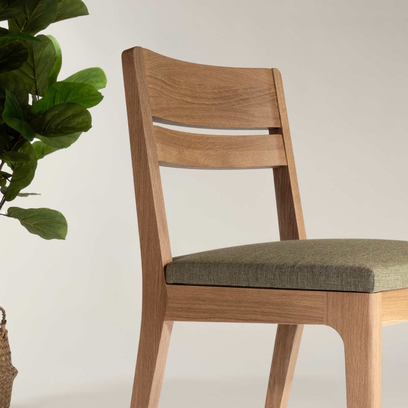 May include: A wooden chair with a light brown finish and a green fabric seat. The chair has a simple design with a curved back and a slatted backrest.