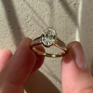 Anillo de compromiso estilo vintage con solitario de corte ovalado y acento de moissanita, bisel completo de diamantes, cuerpo dividido y oro macizo de 14 quilates.