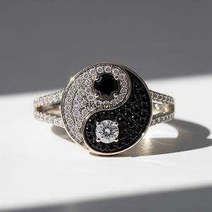 May include: A gold ring with a yin-yang motif. The yin section is black, the yang section is white with clear stones. A black stone is in the centre of the white side, and a clear stone is in the centre of the black side.
