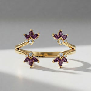 May include: A gold-colored ring with a floral design. Each flower has purple petals and a cluster of small, white gemstones at the center. The ring's band is open, with the brand name "Aksharjewels" visible.