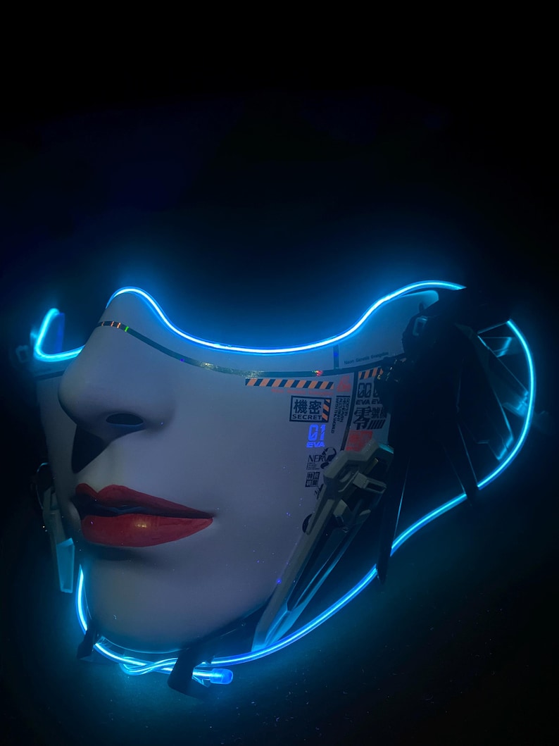 May include: A futuristic mask depicting a woman's face, with red lips and a white face, outlined in neon blue. The mask has Japanese text and mechanical elements, set against a dark backdrop.
