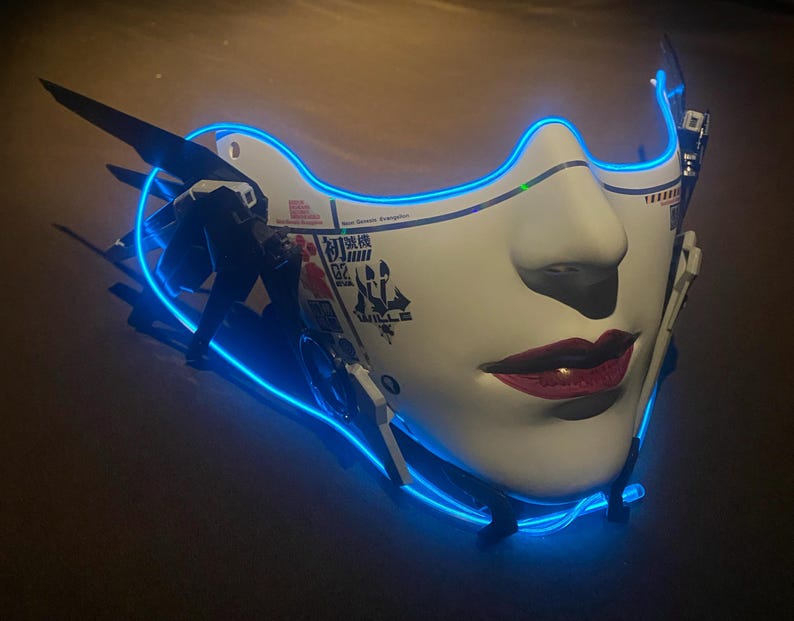 May include: A white futuristic mask with a neon blue outline, depicting a stylized face. The mask features red lips and black accents, with Japanese text and mechanical details. The design evokes a cyberpunk or science fiction aesthetic.