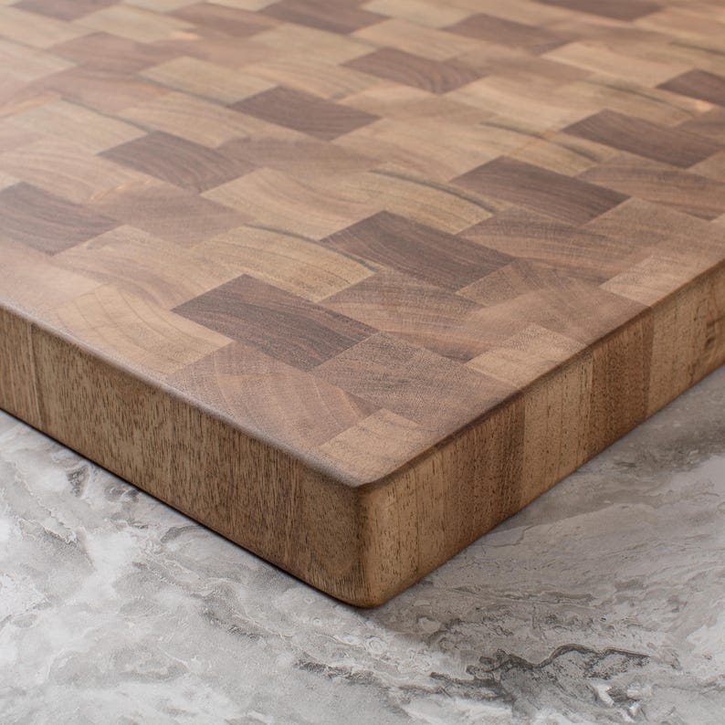 May include: A large, rectangular, wooden chopping board made of walnut wood. The board has a checkered pattern and a smooth, finished surface.