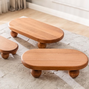 May include: Three wooden oval serving trays with rounded legs. The trays are made of light brown wood and have a smooth, polished surface. The legs are also made of wood and are a darker shade of brown.