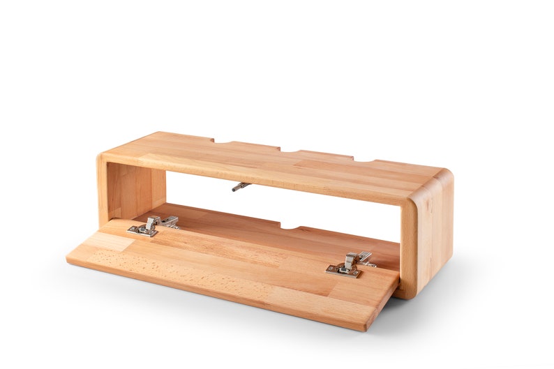 May include: A light wood shelf unit with a hinged front panel that opens to reveal an empty storage space. The shelf unit has a rounded edge and is designed to be mounted on a wall.