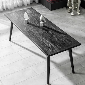 May include: A black wooden coffee table with a rectangular top and four black legs. The table is sitting on a white tiled floor. Two small white bird figurines are placed on the table.