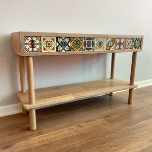 May include: A wooden console table with a single shelf and two legs. The top shelf has a decorative tile design with colourful geometric patterns.