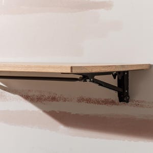 Pu&ograve; includere: Uno scaffale pieghevole in legno con staffe in metallo nero. Lo scaffale &egrave; montato a parete ed &egrave; in posizione abbassata.