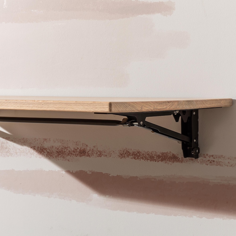 Pu&ograve; includere: Uno scaffale pieghevole in legno con staffe in metallo nero. Lo scaffale &egrave; montato a parete ed &egrave; in posizione abbassata.
