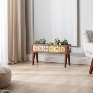 May include: A wooden planter box with a colorful tile design and four legs. The planter is filled with green succulents.