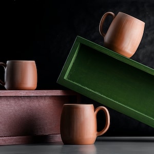 May include: Three terracotta mugs on wooden boxes. One mug is on a green box, and two mugs are on a brown box.