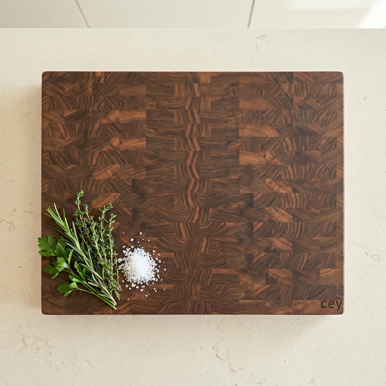 May include: A rectangular end-grain butcher block cutting board with a dark brown wood pattern. Fresh herbs and a pile of salt are arranged on the board. The bottom right corner has the word "cey" printed on it.