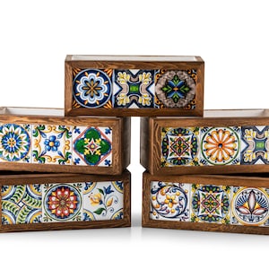 May include: Six rectangular wooden planters with colorful, patterned ceramic tile fronts. The tiles feature floral and geometric designs in blue, yellow, green, and orange. The planters are arranged in a stacked configuration.
