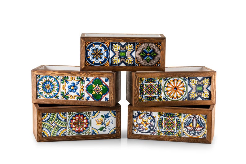 May include: Six rectangular wooden planters with colorful, patterned ceramic tile fronts. The tiles feature floral and geometric designs in blue, yellow, green, and orange. The planters are arranged in a stacked configuration.