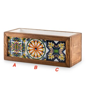 May include: A rectangular wooden planter box with three decorative ceramic tiles. The tiles feature colorful floral and geometric patterns in shades of blue, yellow, orange, and green. The interior of the box is white.