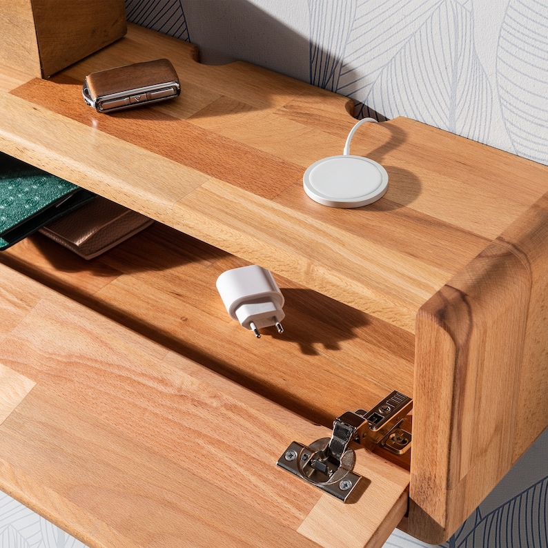 May include: A wooden shelf with a hidden compartment, featuring a wireless charging pad, a phone charger, and a wallet. The shelf is made of light wood with a natural finish.