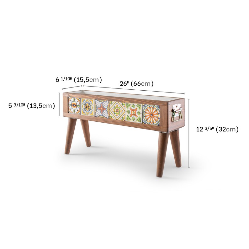 May include: A wooden planter box with a colorful tile design and metal handles. The planter is 26 inches long, 6 1/10 inches wide, and 12 3/5 inches tall. It has four wooden legs.