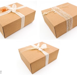 Puede incluir: Tres cajas de regalo de cart&oacute;n marr&oacute;n con diferentes elementos decorativos. La primera caja est&aacute; atada con una cinta blanca y decorada con bayas naranjas. La segunda caja est&aacute; decorada con encaje blanco y cordel. La tercera caja est&aacute; decorada con una cinta blanca y una espiga de trigo.