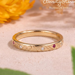 May include: A gold band ring featuring an engraved celestial pattern with a crescent moon, stars, and alternating inset round-cut red rubies and clear white diamonds. The ring is positioned horizontally, showcasing the intricate metalwork and stones.