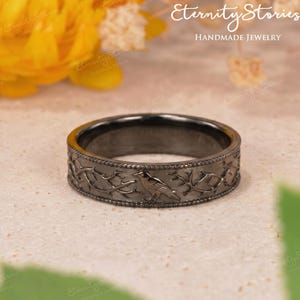 May include: A dark gray ring with a detailed design of a bird and branches. The ring is made of metal and has a matte finish. The words "Eternity Stories Handmade Jewelry" are in the background.