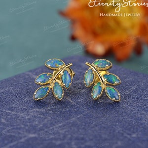 May include: A pair of gold leaf earrings with opal stones. The earrings are in the shape of a branch with five leaves. The opal stones are a mix of blue, green, and purple.