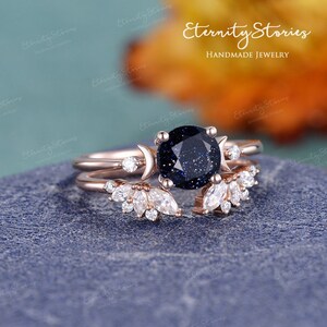 May include: A rose gold ring set with a blue gemstone surrounded by smaller clear gemstones. The ring features a crescent moon design and a delicate floral pattern.