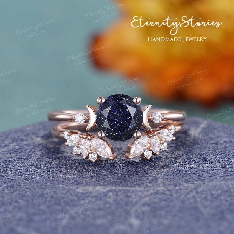 May include: A rose gold engagement ring set with a blue starry sky gemstone and a crescent moon design. The ring is set with smaller diamonds on the band and the crescent moon.