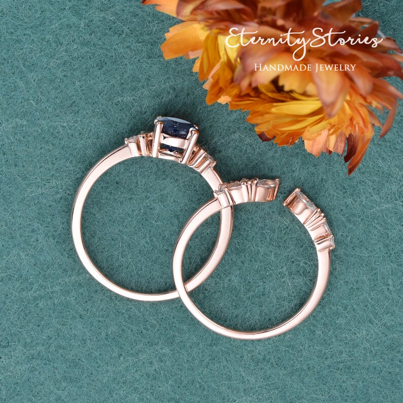 May include: Two rose gold rings with a blue gemstone and clear stones. The rings are set on a green background. Eternity Stories Handmade Jewellery.