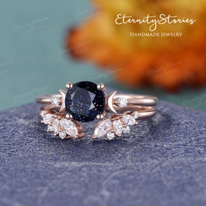 May include: A rose gold ring set with a blue starry sky stone, two crescent moons, and a delicate leaf design. The ring is handmade and features a unique and celestial design.
