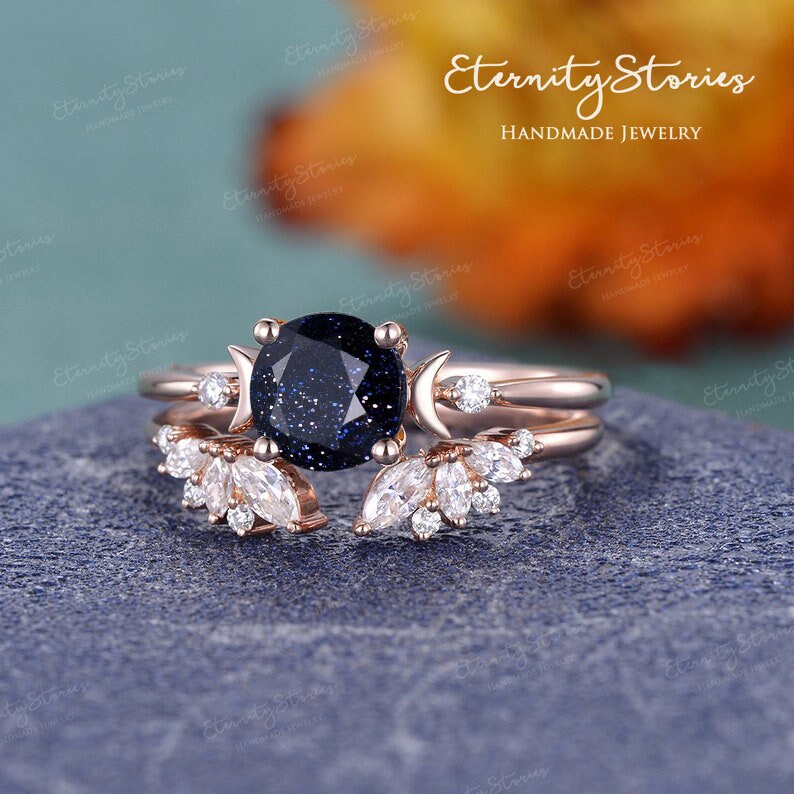 May include: A rose gold ring set with a blue starry sky stone, two crescent moons, and a delicate leaf design. The ring is handmade and features a unique and celestial design.